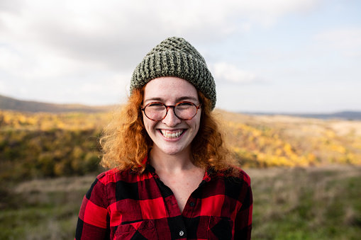 Beautiful young woman with red curly hair posing for the camera. Carefree redhead woman smiling and enjoying her weekend getaway to the mountain.