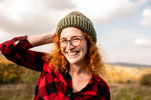 Beautiful young woman with red curly hair posing for the camera. Carefree redhead woman smiling and enjoying her weekend getaway to the mountain.