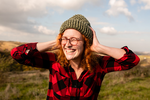 Beautiful young woman with red curly hair posing for the camera. Carefree redhead woman smiling and enjoying her weekend getaway to the mountain.