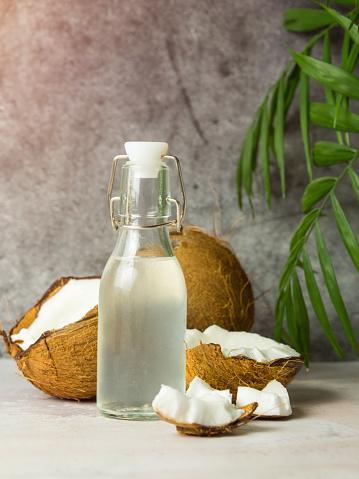 fresh refreshing Coconut water in a bottle with an open coconut with white pulp on a concrete background.