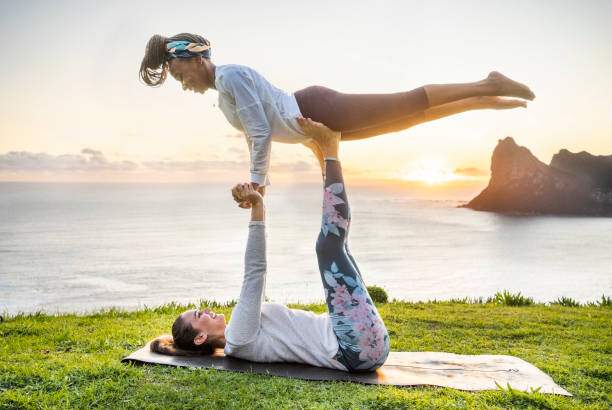 Two fitness women doing acro yoga exercises in morning Two fitness women doing acro yoga exercises on mountain along the sea in morning acroyoga stock pictures, royalty-free photos & images