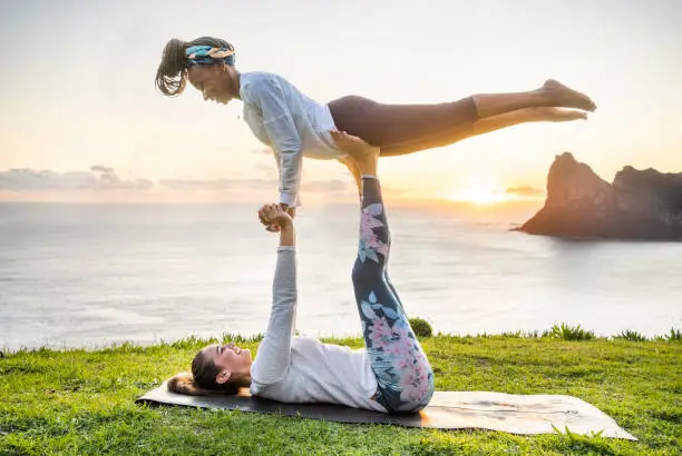Two fitness women doing acro yoga exercises on mountain along the sea in morning