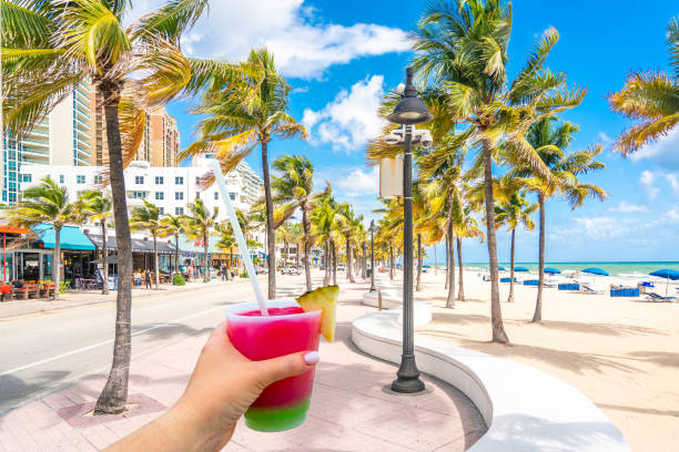 Seafront beach promenade with hand holding cocktail and palm trees on background on sunny day in Fort Lauderdale in Florida USA stock photo