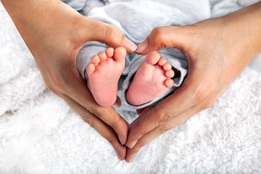 Newborn baby girl in pink knitted hat on a bed.