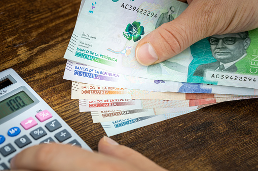 Hombre sostiene pesos colombianos en mano y cuenta con calculadora de gastos o ganancias, concepto financiero, presupuesto de casa de los colombianos photo