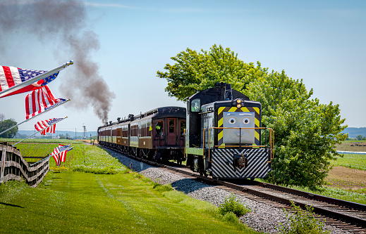 Strasburg, Pennsylvania. June 48 2021 - View of Thomas the Train Pulling Passenger Cars While Passing American Flags on a Fence on a Sunny Day