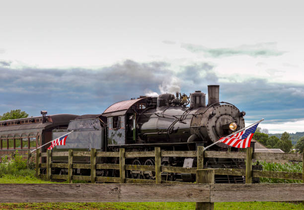 istock American Flags are Waving in the Wind, on a Fence, While a Steam Passenger Train Approaches 1441519080