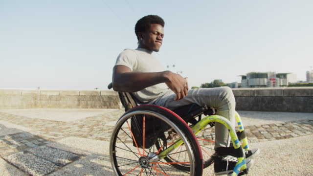 Happy African American man dancing using wheelchair outdoors