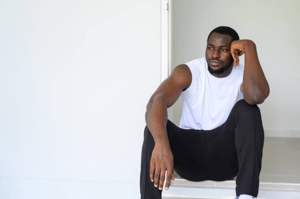 Portrait of pensive African American man sitting and looking outside the home. Portrait of pensive African American man sitting and looking outside the home poor house exterior stock pictures, royalty-free photos & images