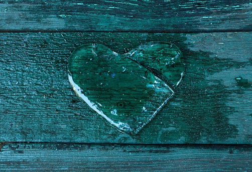 Broken heart. Icy heart, transparent and split against a background of green wooden boards. Ice Valentine. Abuse, end of love