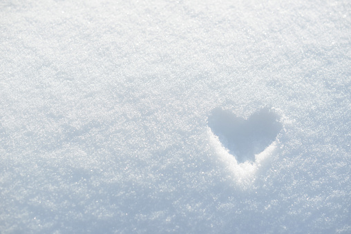 Drawing of a heart in the snow. Frozen heart painted on white snow background. Heart shape, ice or snowy valentine