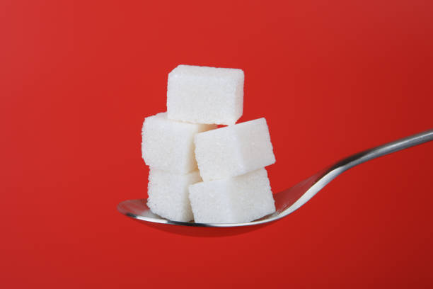 heap of white sugar cubes in the spoon isolated on red background