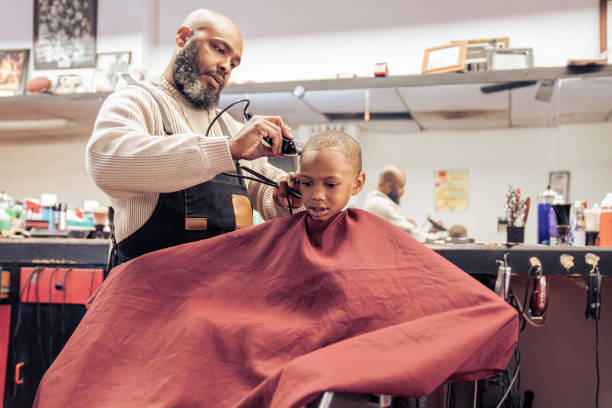 Black customers receive a haircut from barbers at a Black owned Barbershop A Black woman, young child, teenager, and adult male receives a haircut and a line-up from a classic barbershop. black barber stock pictures, royalty-free photos & images
