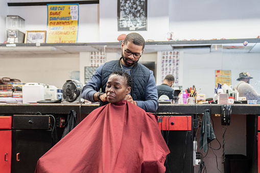 A Black woman, young child, teenager, and adult male receives a haircut and a line-up from a classic barbershop.