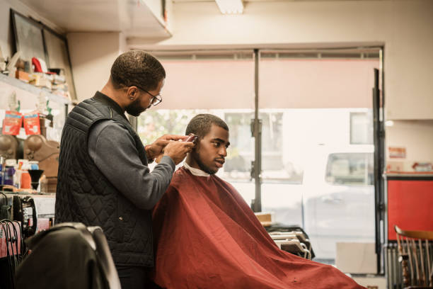 Black customers receive a haircut from barbers at a Black owned Barbershop A Black woman, young child, teenager, and adult male receives a haircut and a line-up from a classic barbershop. black barber stock pictures, royalty-free photos & images