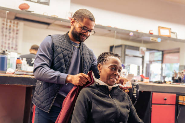 Black customers receive a haircut from barbers at a Black owned Barbershop A Black woman, young child, teenager, and adult male receives a haircut and a line-up from a classic barbershop. black barber stock pictures, royalty-free photos & images