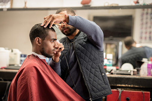 A Black woman, young child, teenager, and adult male receives a haircut and a line-up from a classic barbershop.
