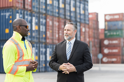 Senior male supervisor and african american male engineer discussing, working at container terminal. Inspector or supervisor in container terminal. Ship, port, container and cargo industry