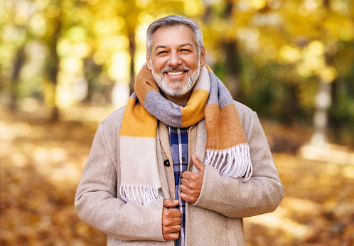 Portrait of happy positive mature man with broad smile    in elegant clothes on an autumn walk   in city park
