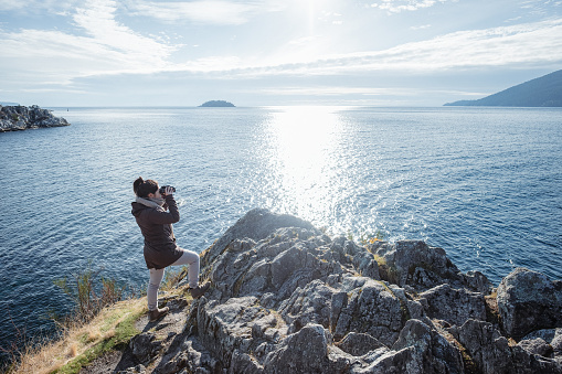 Eurasian young woman birdwatching from rocky viewpoint at Whytecliff Park, West Vancouver, British Columbia, Canada.