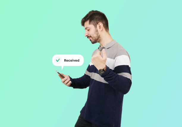istock Money Received. Young Pakistani guy holding mobile and posing in a winning gesture with side pose. Happy Male received payment on mobile wearing strips shirt Facebook post. Guy with mobile cell phone. 1441564853