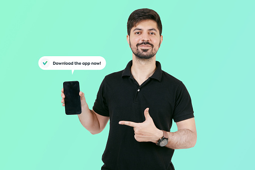Happy Guy having smart phone with black screen in hand, pointing with forefinger to product. Guy holding mobile and asking to download the app now. Happy Indian guy showing mobile screen.