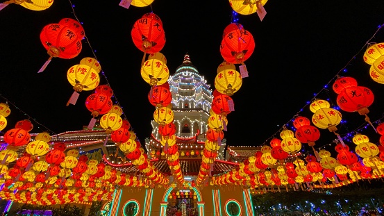 A low-angle shot of red and yellow lanterns under the night sky during the Chinese New Year with an illuminated building in the background