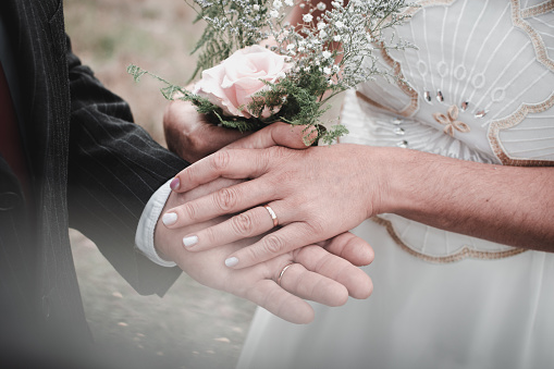 A closeup of a newly married couple holding hands in a park