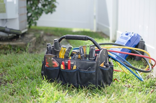 Orlando, United States – November 10, 2022: A tool bag full of different tools for a ac mechanic on the grass with a fence on the background
