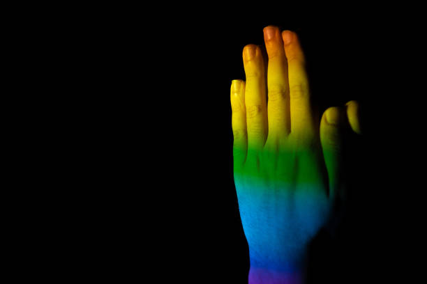 A closeup of praying hands illuminated with the LGBT pride flag on a black background with space for your text - peace concept