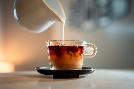 A close-up shot of a poring milk in a hot tea.