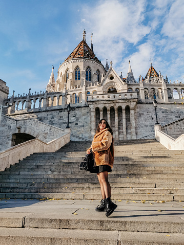 Portrait of beautiful young woman wearing stylish winter clothes, standing on stairs in front of Fisherman's bastion in Budapest, Hungary