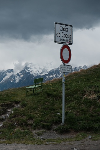 A vertical shot of sign post at Col of Croix de Coeur with bench and dark Clouds