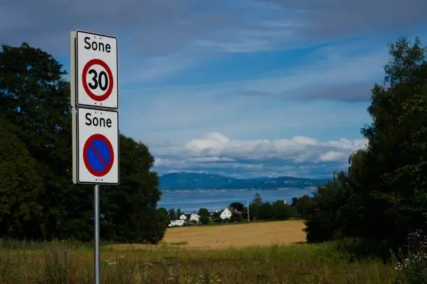 The Norwegian roadsigns with houses on the shoreline under a blue cloudy sky in Trondheim, Norway.