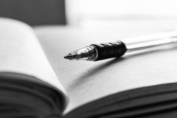 istock Grayscale closeup shot of a pen on an open notebook 1441577336