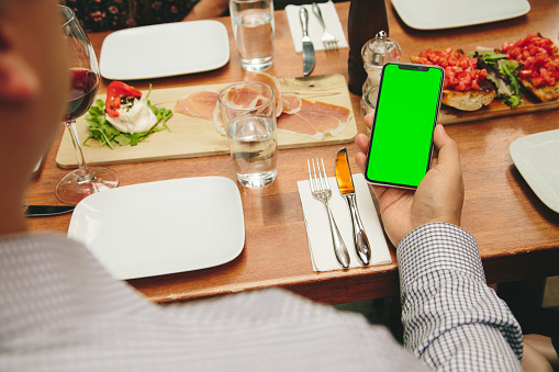 A man checking his phone with a green screen on a dinner table