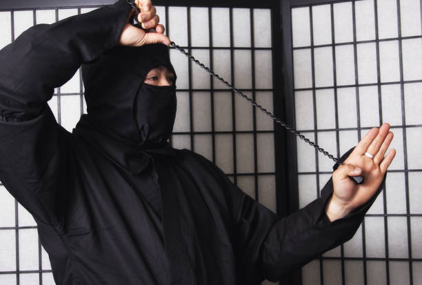 An Asian man wearing ninja costume and holding weapons