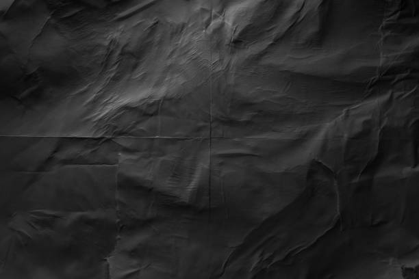 Heavy crumpled black paper texture in low light background stock photo