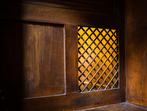A closeup of a wooden window of the confessional box at church