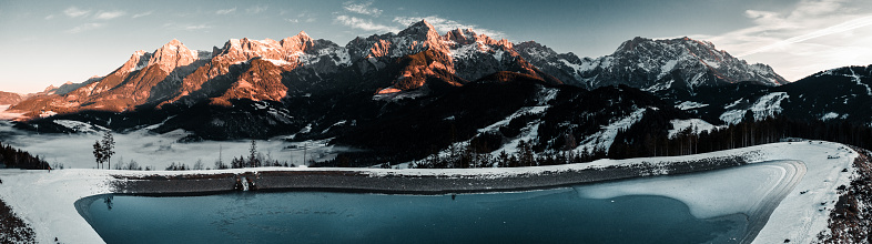 A panoramic shot of a frozen lake surrounded by rocky mountains covered in the snow in the countryside