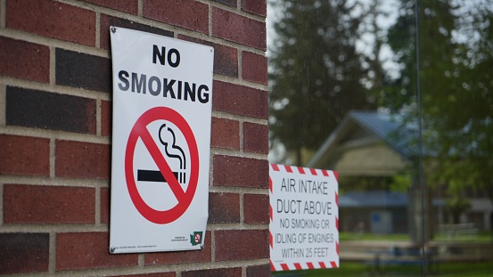 A closeup of a No smoking warning sign on a brown brick wall on the streets