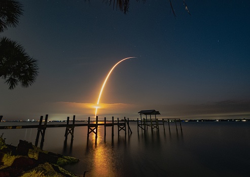 A beautiful shot of a wooden pier on the lakeshore with a missile launch at dawn sky in the background