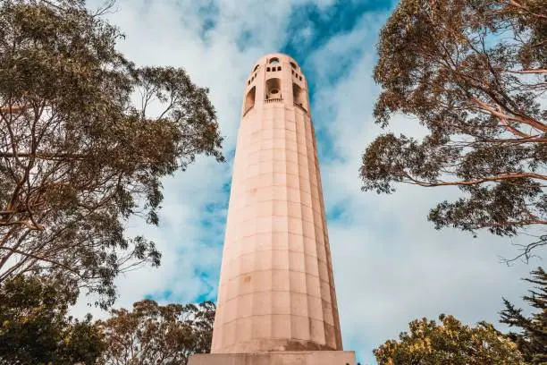 Photo of Low angle shot of the Coit Tower in San Francisco, California, USA with trees and a blue cloudy sky