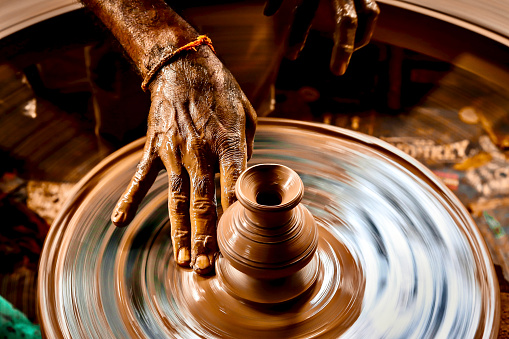 A slow shutter speed shot of a potter hand making a pot from a pottery wheel.