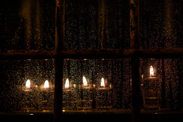 Hanukkah candles seen through a window wet with rain Vials of oil and burning wicks in a menorah glow brightly in a window on a rainy night in Jerusalem during the Jewish festival of Hanukkah. showers of blessings stock pictures, royalty-free photos & images
