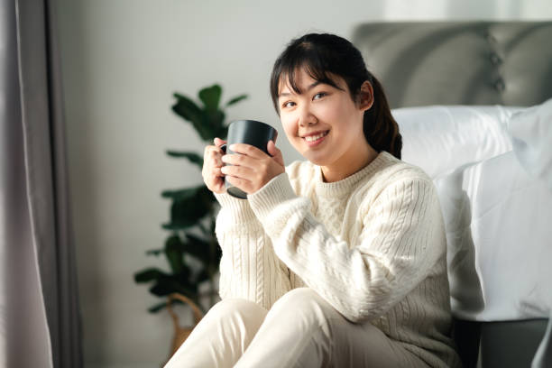 istock Young woman drinking coffee in bedroom, Holding coffee cup with two hands 1441589486