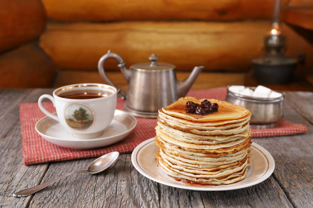 Pancakes for tea party in retro style. On an old wooden table against a log wall is a stack of pancakes on a ceramic plate next to vintage utensils for tea party. tea party horizontal nobody indoors stock pictures, royalty-free photos & images
