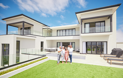 Portrait of happy family moving into their new luxury home, house or property in summer. Parent, grandparents and girl standing on the grass, lawn, backyard or garden with a smile   together