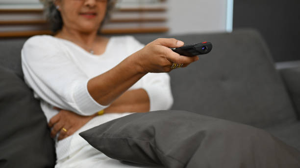 istock Happy senior woman using remote controller to switch channels, watching favorite movie online series in living room. 1441595532