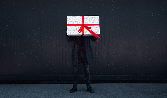 Unrecognizable shy man standing outdoors with a big wrapped gift box.